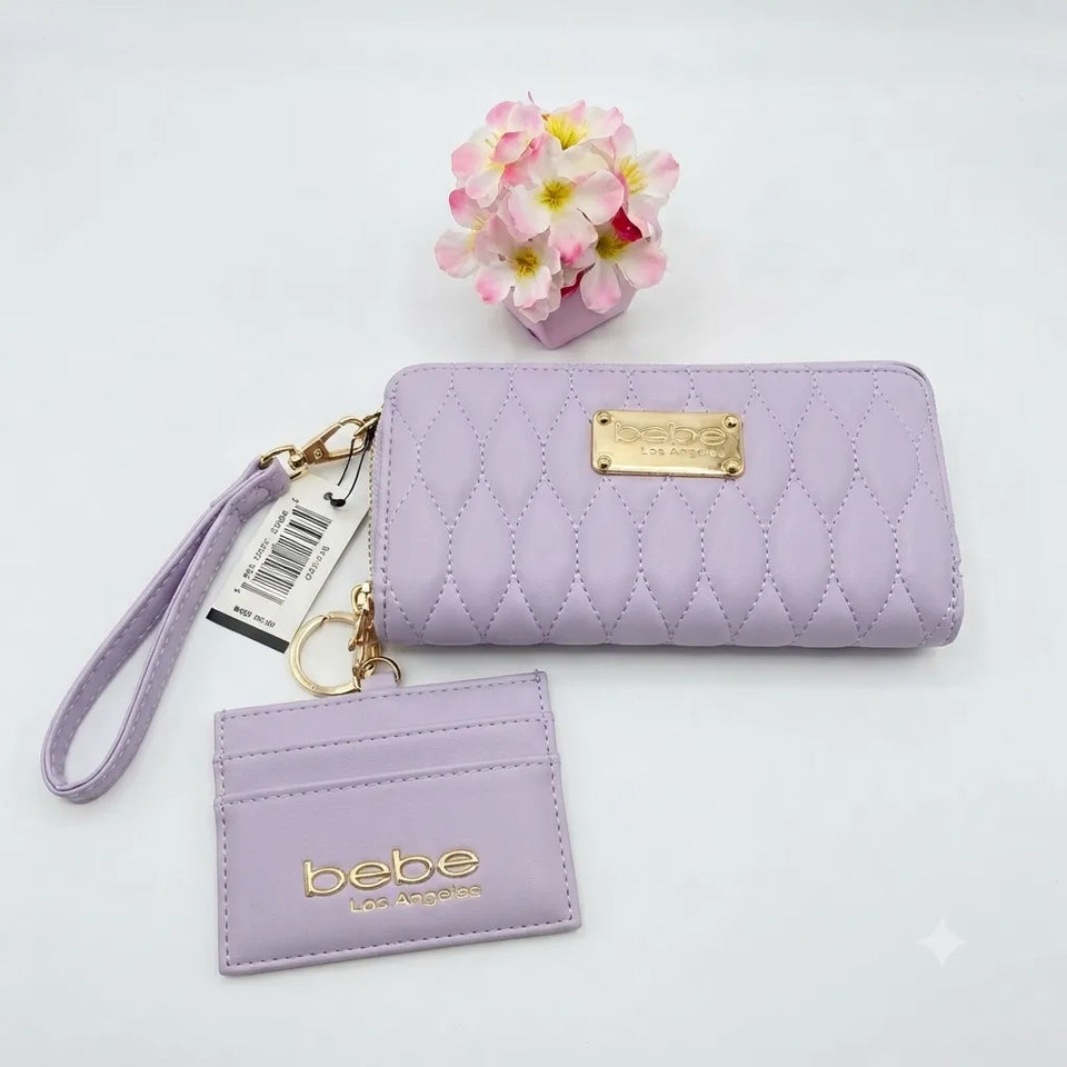 A light purple quilted wallet set with a wristlet strap and a matching card holder, featuring gold-tone hardware and a gold 'bebe' logo plaque, displayed on a white background with a small pink flower decoration.