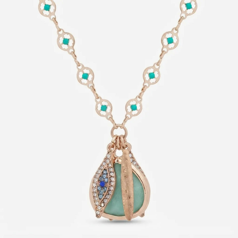 A rose gold necklace with a teardrop pendant featuring a light green stone, blue gem accents, and small clear crystals, shown on a light gray background.
