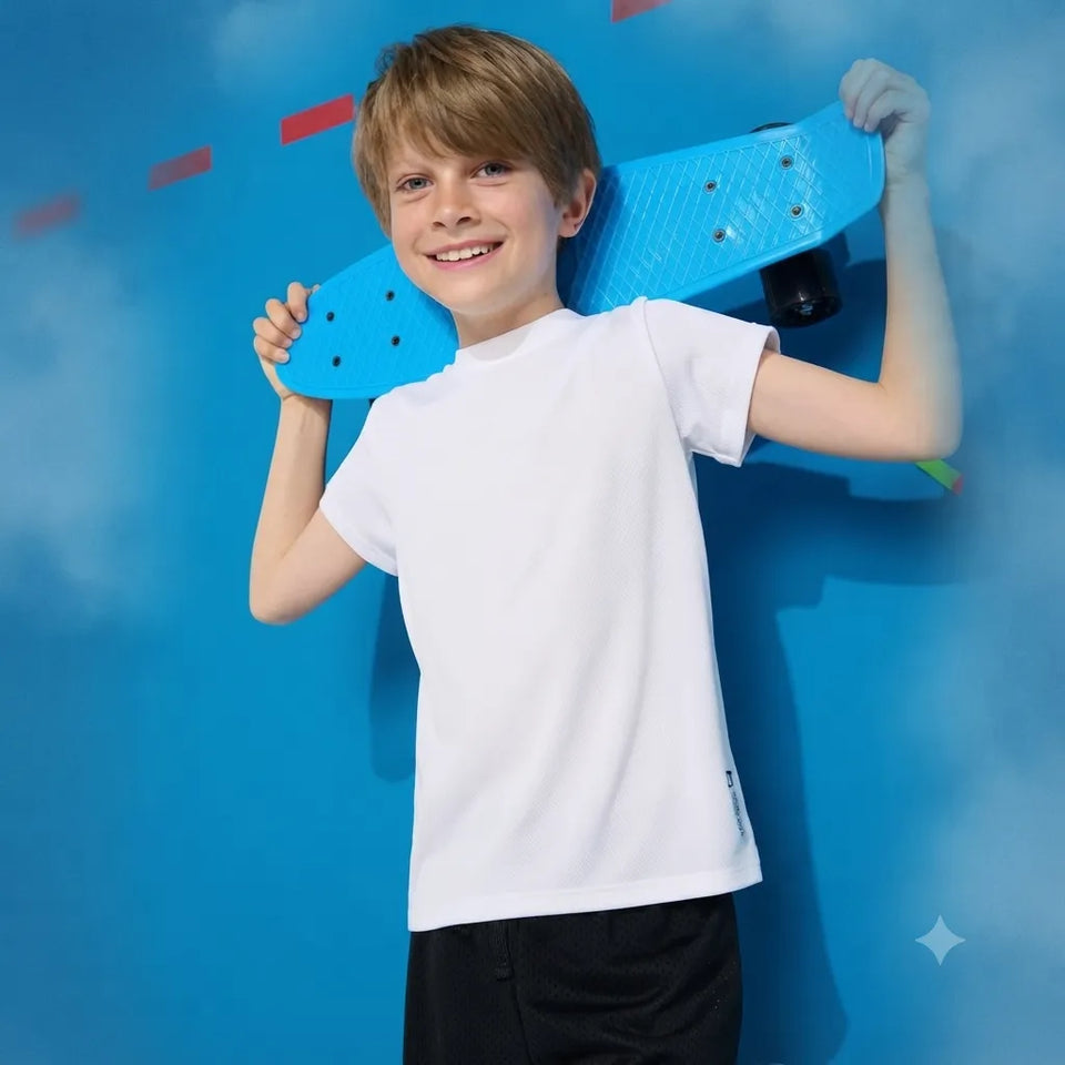 A smiling young boy with light brown hair stands against a bright blue background, holding a light blue penny board over his shoulder. He is wearing a plain white short-sleeve t-shirt and black shorts.
