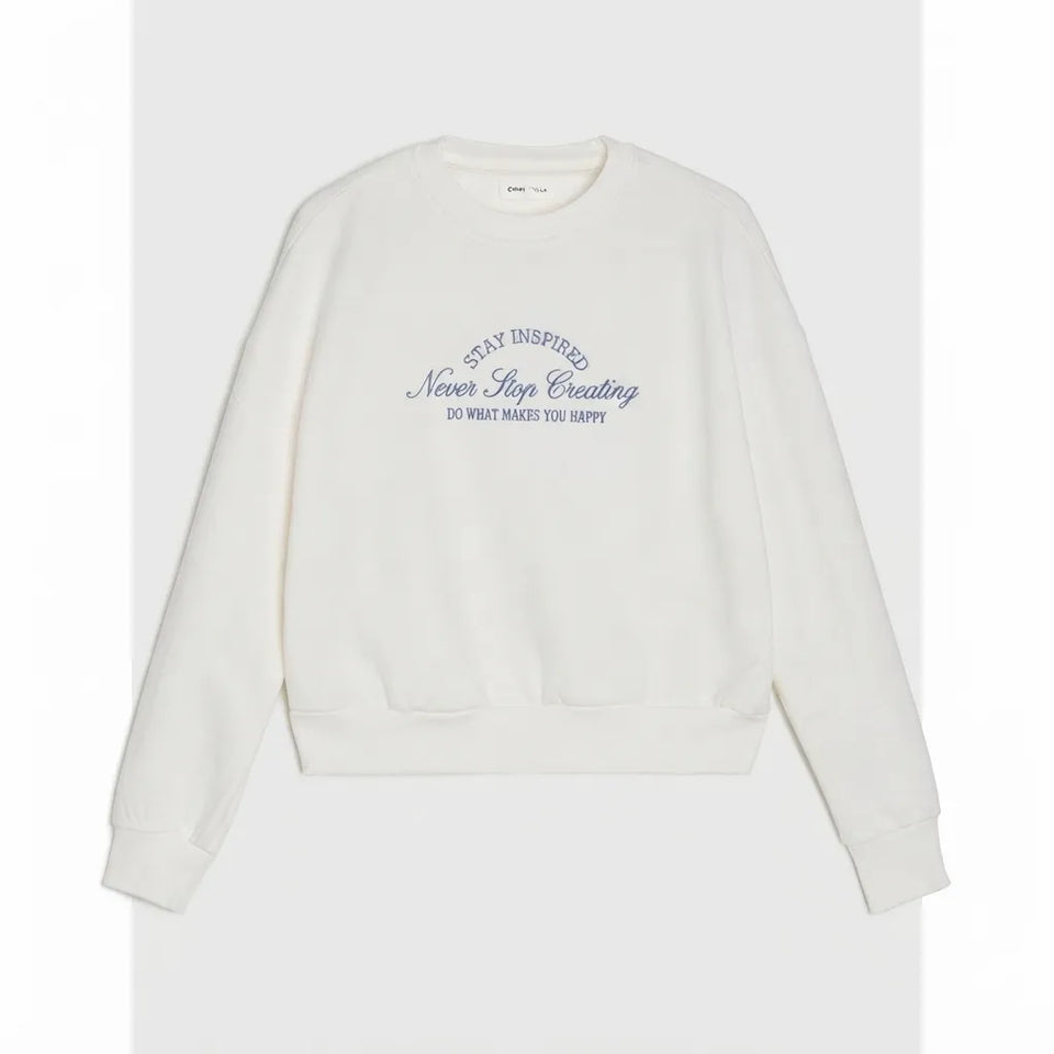 An off-white crewneck sweatshirt with blue text on the chest reading 'NEVER STOP Creating DO WHAT MAKES YOU HAPPY' and 'STAY INSPIRED', displayed against a light gray background.