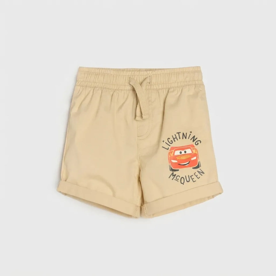 Beige children's shorts featuring a drawstring waist and a graphic print of Lightning McQueen from Disney's Cars on the left leg, displayed against a light gray background.