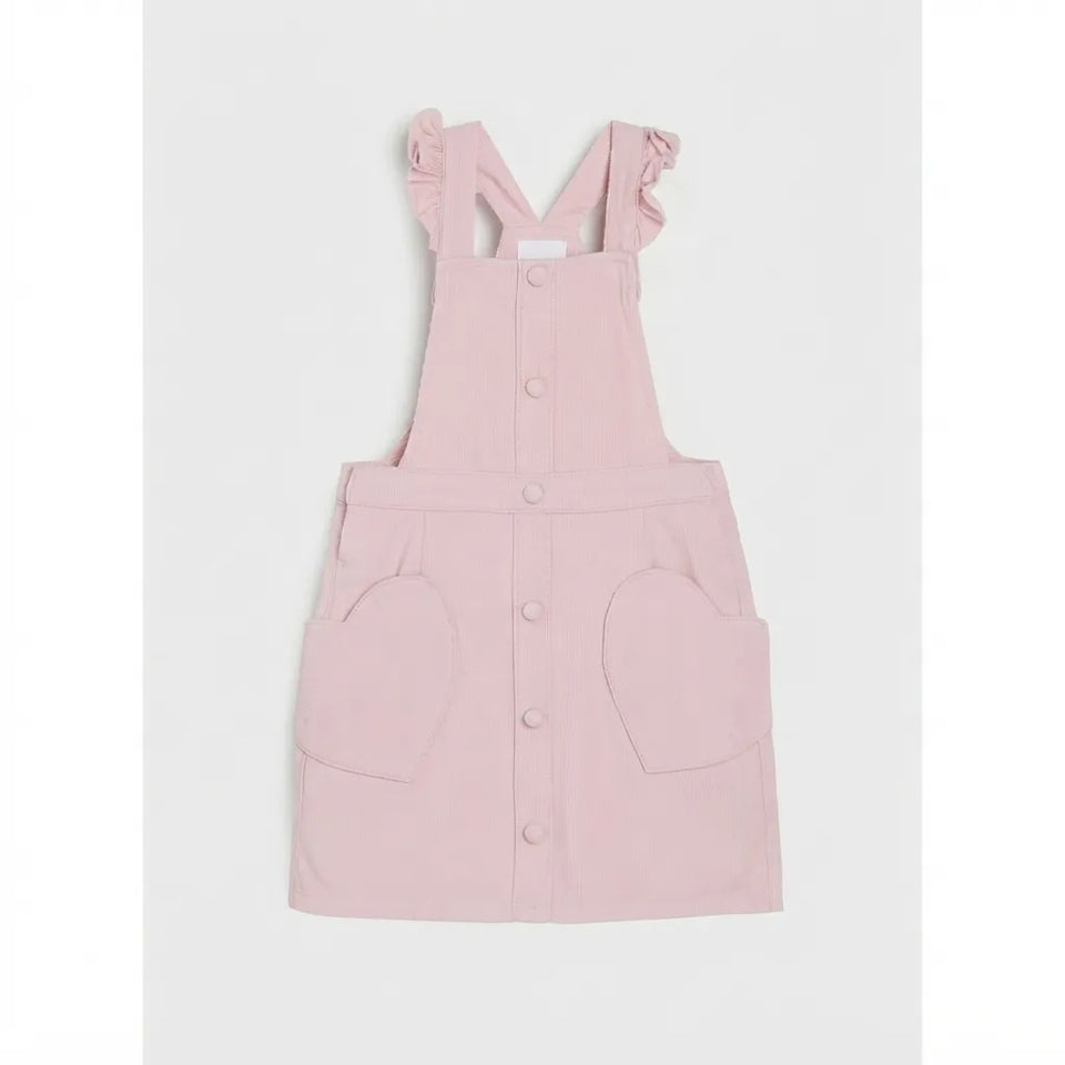A light pink pinafore-style dress with ruffled shoulder straps, a button front, and large front patch pockets, shown flat against a light gray background.