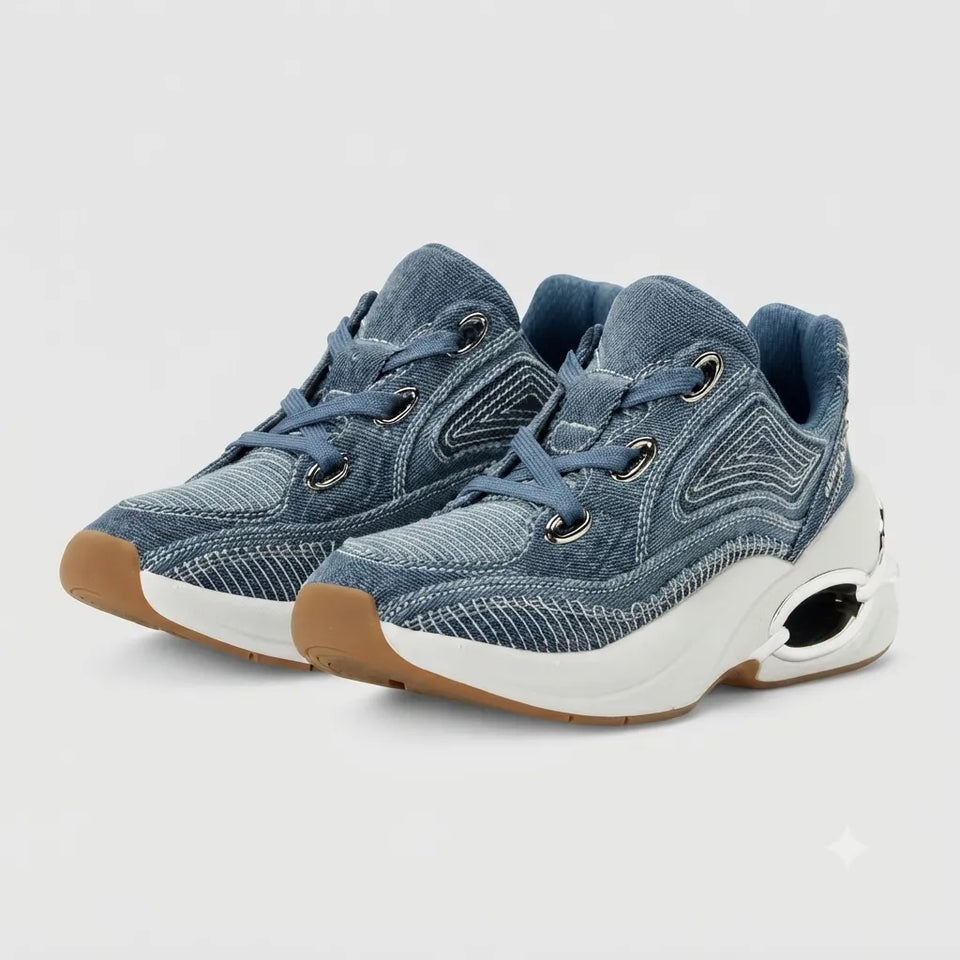 A pair of low-top sneakers with a blue denim-like textured upper, blue laces, a thick white midsole with a visible air pocket, and a gum brown outsole, shown on a light gray background.