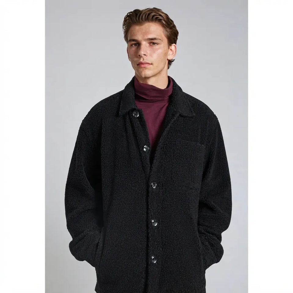 A man wearing a black textured teddy fleece button-up coat over a burgundy turtleneck sweater, photographed against a neutral gray studio background.
