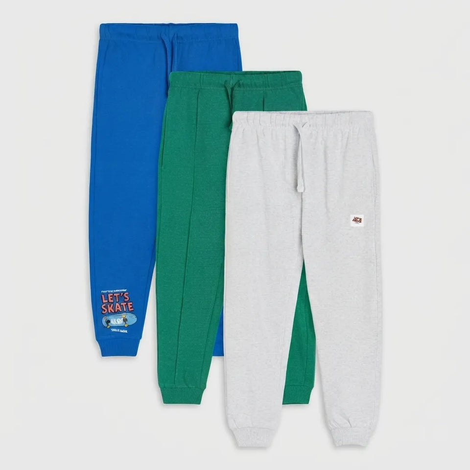 Three pairs of kids' jogger sweatpants in blue, green, and light gray, arranged in a vertical stack on a light gray background. The blue pair features a 'LET'S SKATE' graphic on the lower left leg.