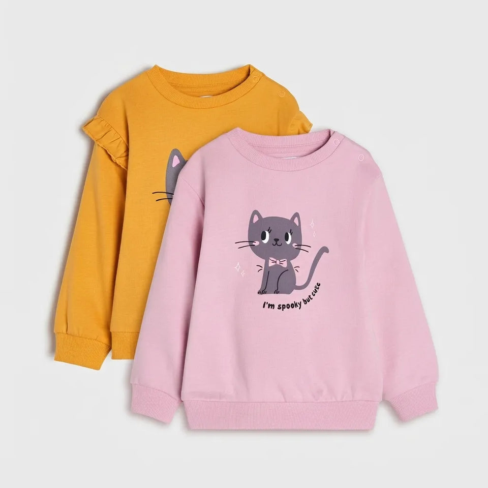 Two children's long-sleeve sweatshirts shown on a light gray background: one in mustard yellow with a partial gray cat graphic, and one in light pink with a full gray cat graphic and the text 'I'm spooky about.'.