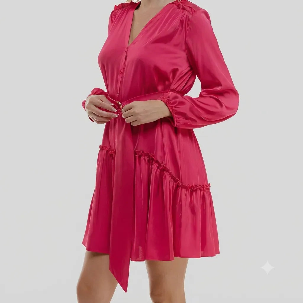 A woman wearing a bright pink satin mini dress with long sleeves, a V-neckline, and a matching self-tie belt, shown against a plain light gray studio background.