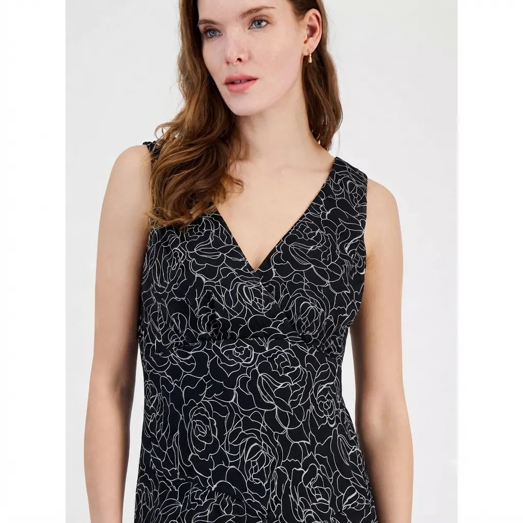 A woman wearing a sleeveless V-neck dress with a black base and white rose line pattern, photographed against a plain light gray studio background.