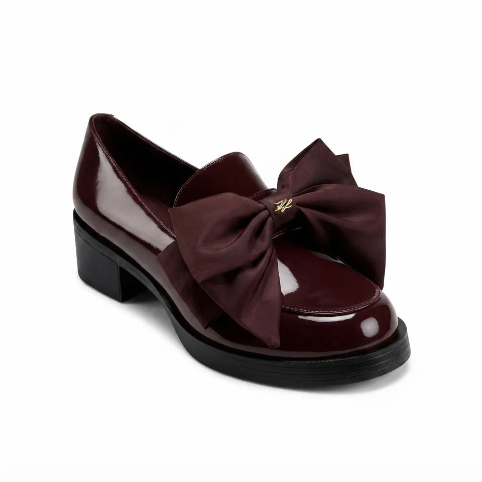 A single women's loafer-style shoe in glossy deep burgundy patent leather with a large matching satin bow across the toe and a black block heel, shown on a clean white background.