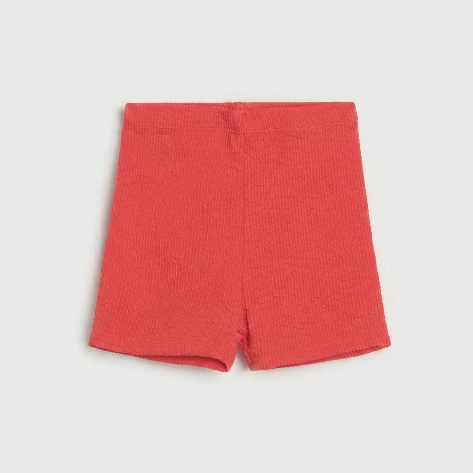 A pair of coral red waffle-knit shorts laid flat against a light gray background.