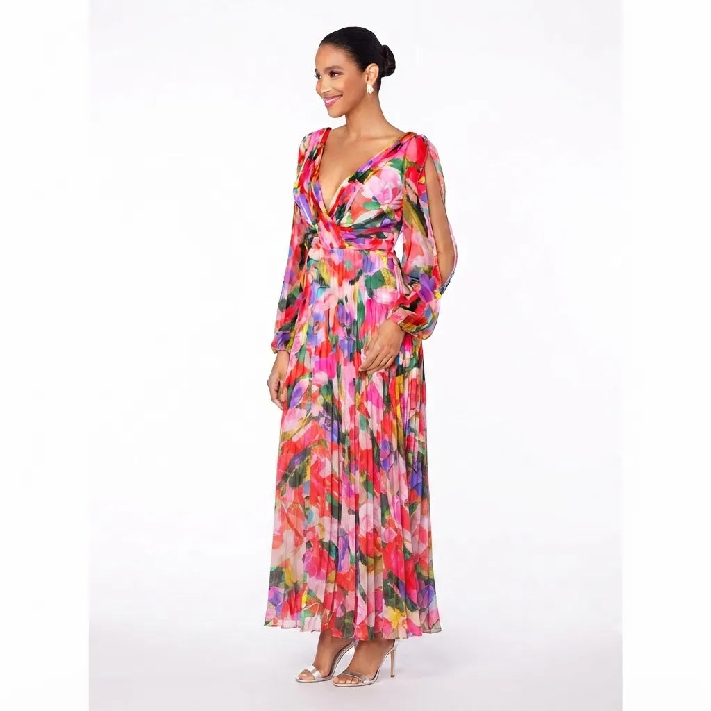 A woman modeling a long-sleeve maxi dress with a vibrant multicolor floral print, featuring a wrap-style V-neck bodice and pleated skirt, set against a plain white studio background.