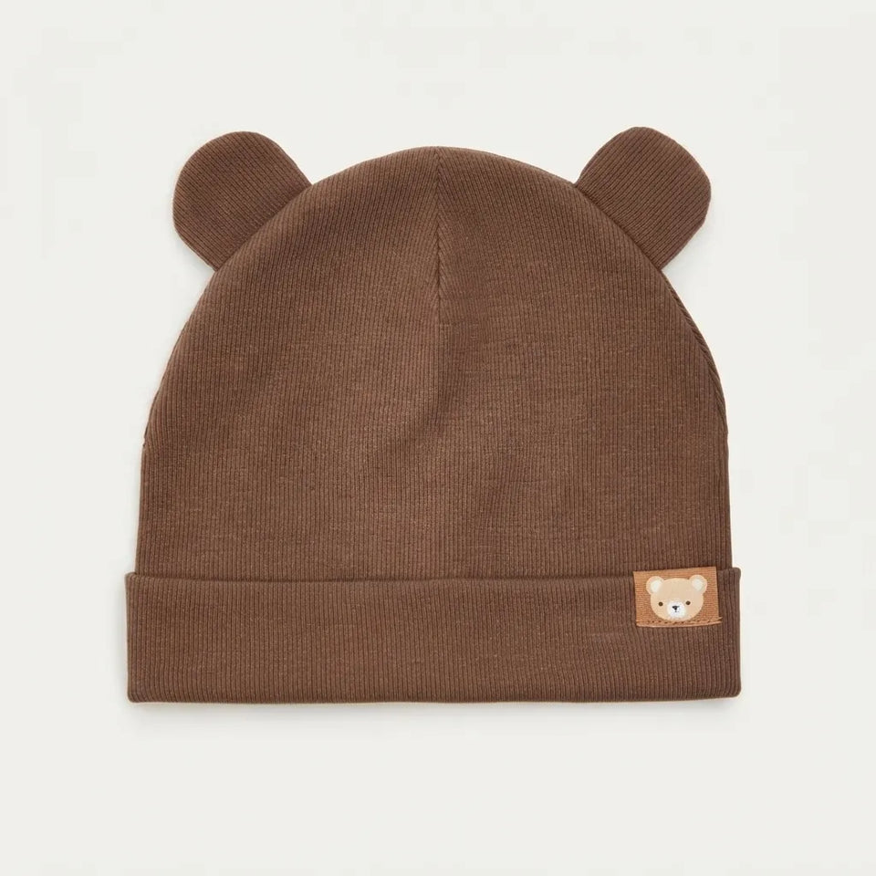 A brown ribbed knit baby beanie hat with small bear ears on top and a small embroidered bear face patch on the cuff, shown against a plain white background.