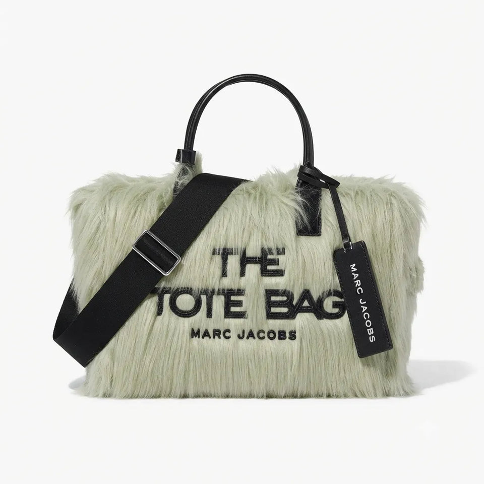 Marc Jacobs 'The Tote Bag' in a pale mint green faux fur material, featuring black leather handles, a black shoulder strap, and black printed text on the front.