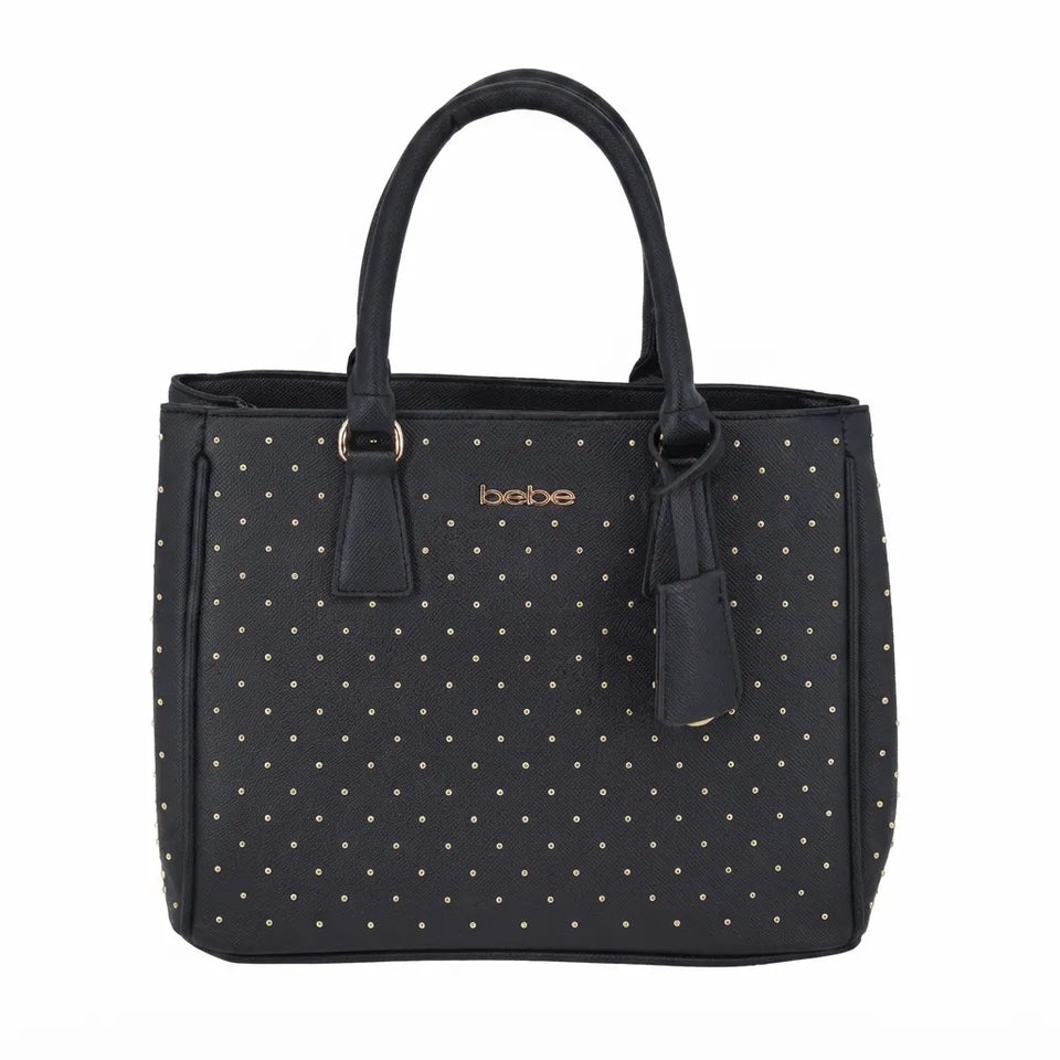 A black tote bag with a gold polka dot pattern, featuring dual top handles, a hanging leather tag, and the brand name 'bebe' printed in gold on the front.