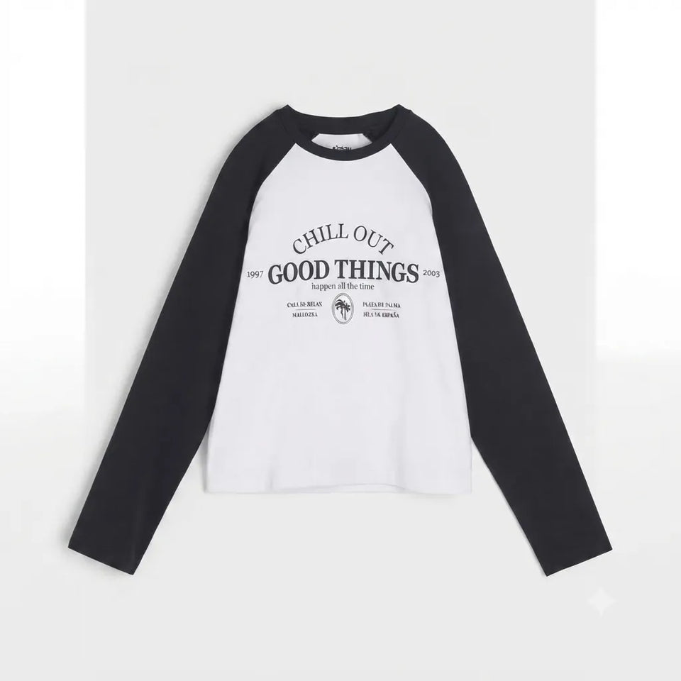 A long-sleeve raglan shirt with a white body and black sleeves, featuring a black graphic print on the front that reads 'CHILL OUT GOOD THINGS' with smaller text and a circular logo.