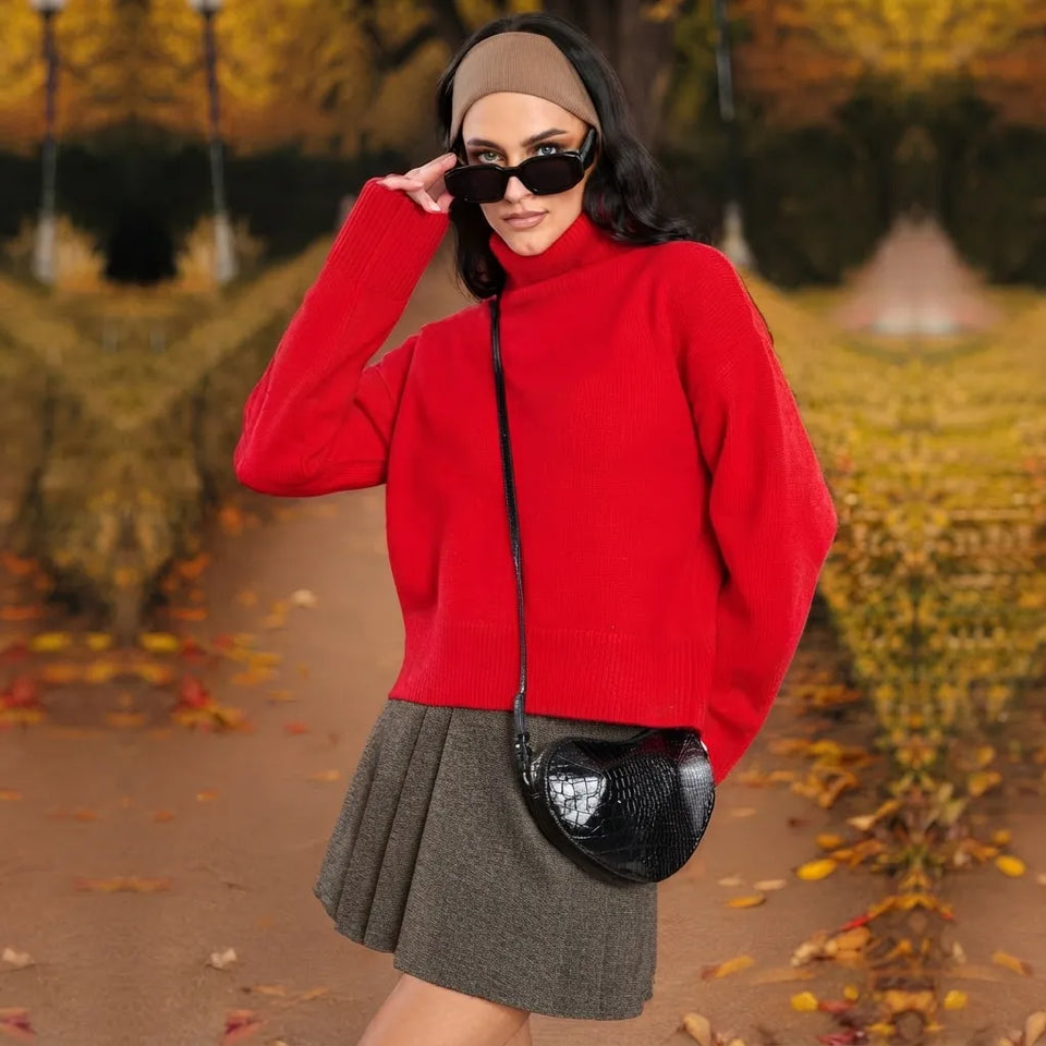 A woman wearing a bright red turtleneck sweater, a gray pleated mini skirt, black sunglasses, and a beige headband, carrying a black crocodile-embossed crossbody bag in an autumn park setting.