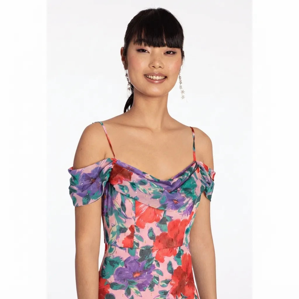 A woman wearing a colorful floral off-the-shoulder dress with thin straps, photographed against a plain light gray studio background.