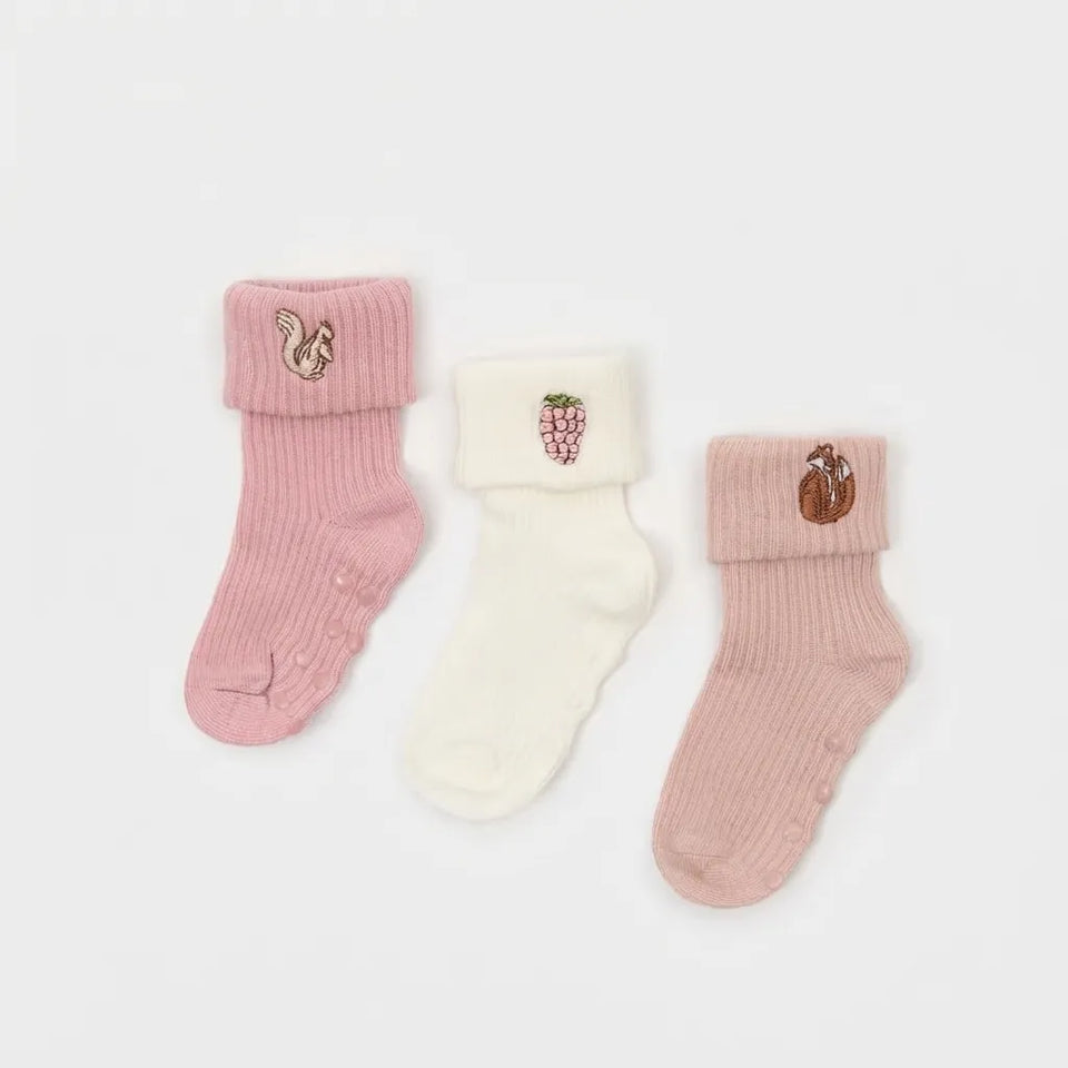 Three pairs of baby socks laid flat on a light gray background: a pink sock with a squirrel patch, an off-white sock with a grape patch, and a dusty pink sock with a peach patch.