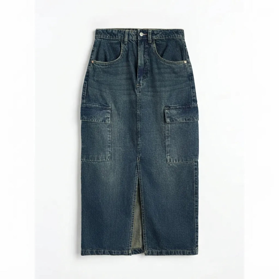 A dark blue denim midi skirt with a front slit, featuring classic five-pocket styling and two large patch pockets on the sides, laid flat against a white background.