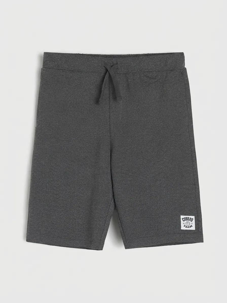 Dark gray heathered sweatshirt shorts with an elastic drawstring waistband and a small white brand patch on the lower left leg, shown flat on a light gray background.
