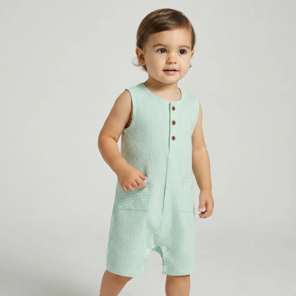 A toddler wearing a sleeveless ribbed romper in a pale mint green color with three brown buttons on the chest, standing against a light gray studio background.