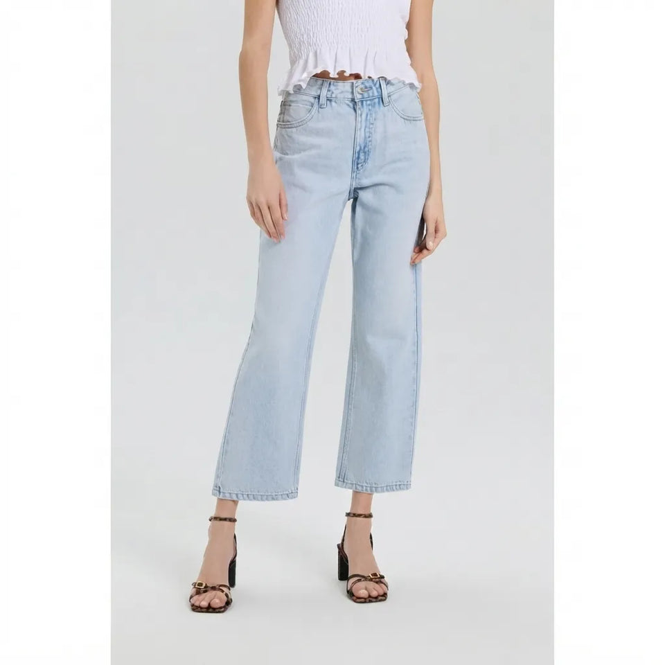 A model wearing light-wash blue cropped wide-leg jeans, paired with a white ruffled top and black strappy heels, shown against a light gray studio background.