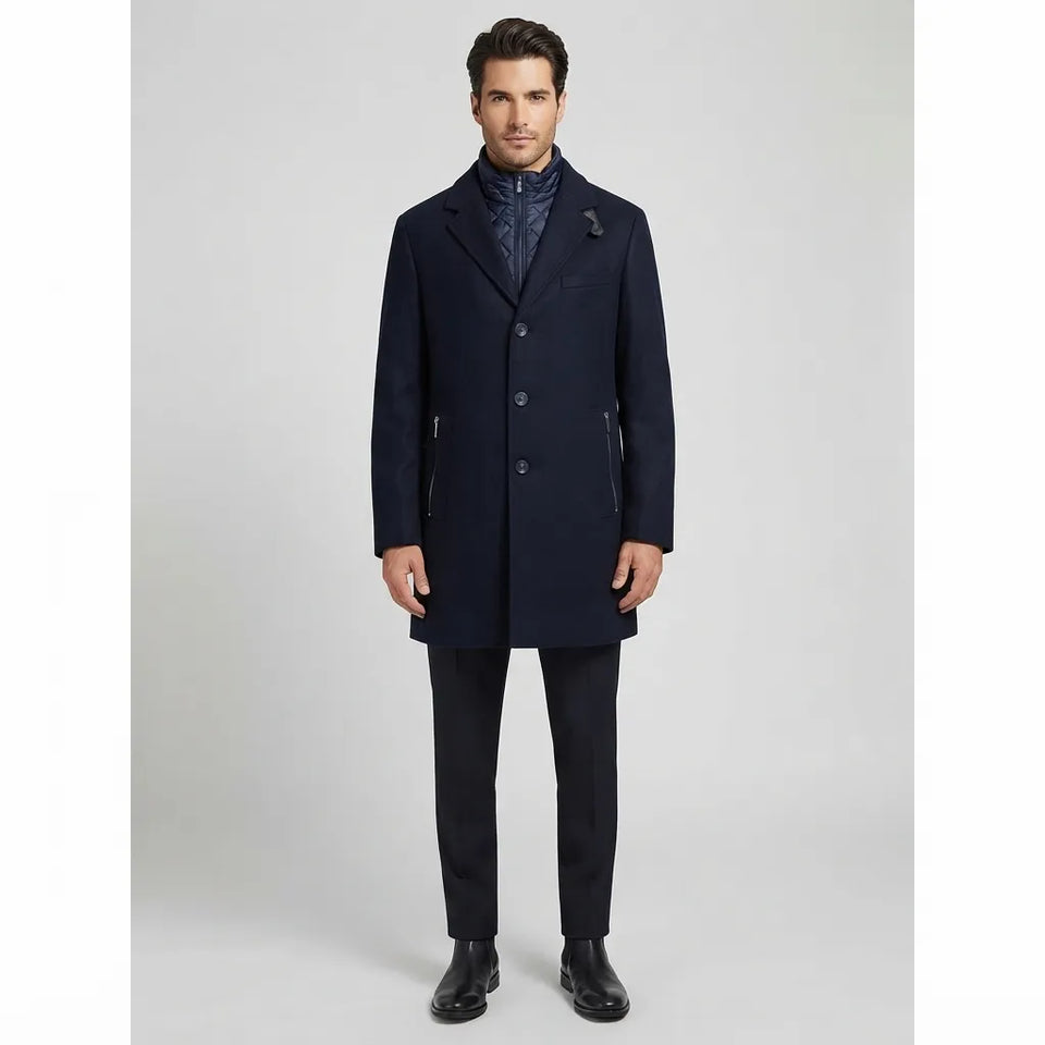 A man modeling a dark navy blue wool-blend coat over a patterned navy shirt, paired with dark trousers and black leather shoes, against a light gray studio background.