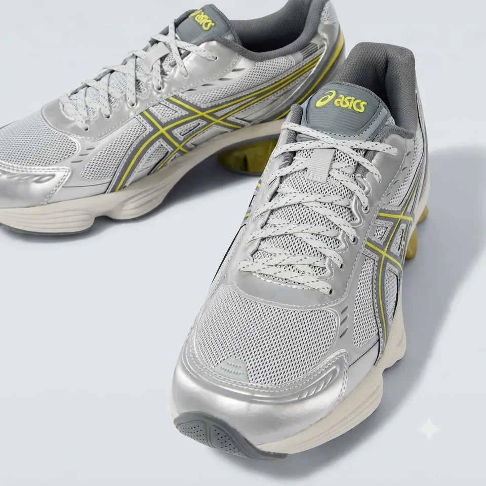 A pair of ASICS athletic sneakers in metallic silver with yellow-green stripe accents and a gray collar, shown on a light gray studio background.