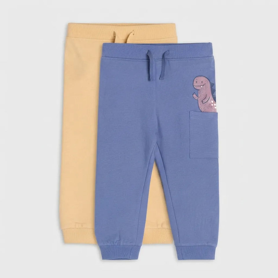 Two pairs of children's sweatpants, one in dusty blue with a dinosaur patch and front pocket, and one in pale yellow, displayed flat against a light gray background.
