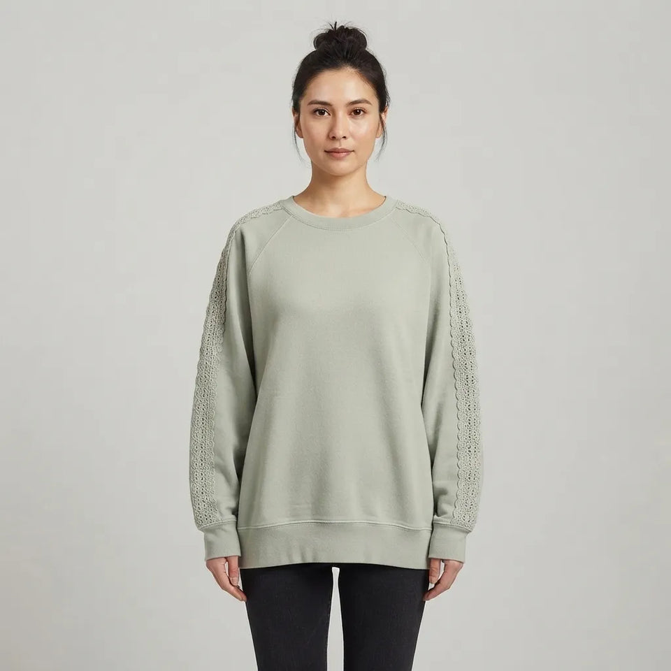 A woman modeling a sage green crewneck sweatshirt with textured lace-knit sleeves, paired with black leggings, against a light gray studio background.