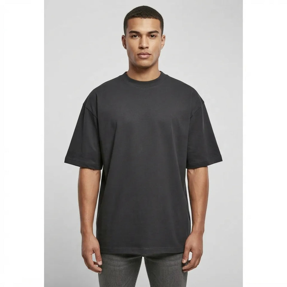 A man wearing an oversized black short-sleeve crewneck t-shirt, standing against a light gray studio background.