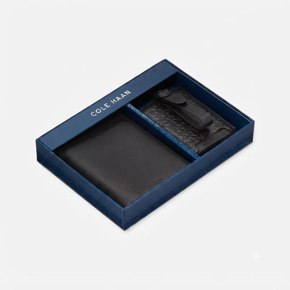 Cole Haan men's gift set featuring a black leather wallet and a black leather cardholder inside an open navy blue presentation box on a light gray background.