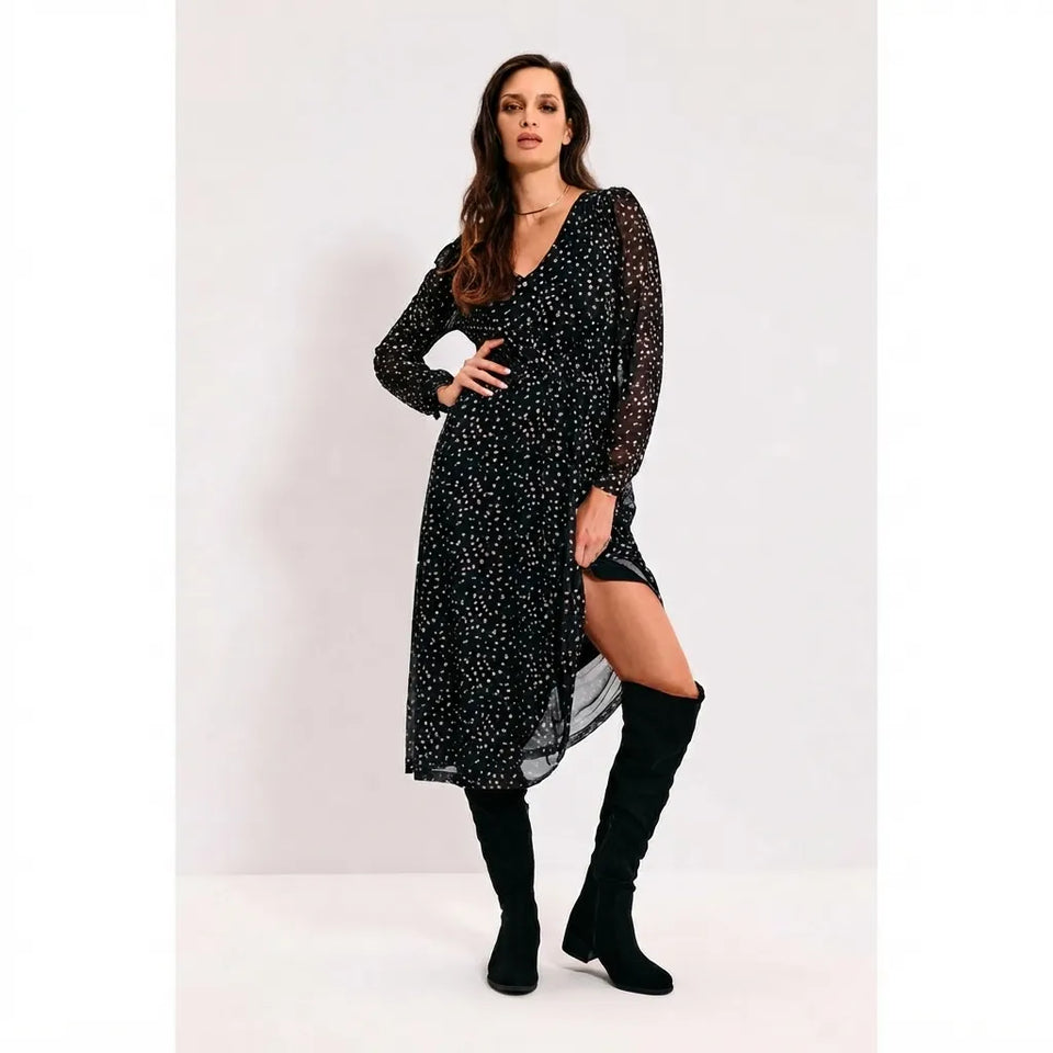 A woman models a black long-sleeve midi dress with a white polka-dot pattern, paired with black over-the-knee boots, against a plain light gray studio background.