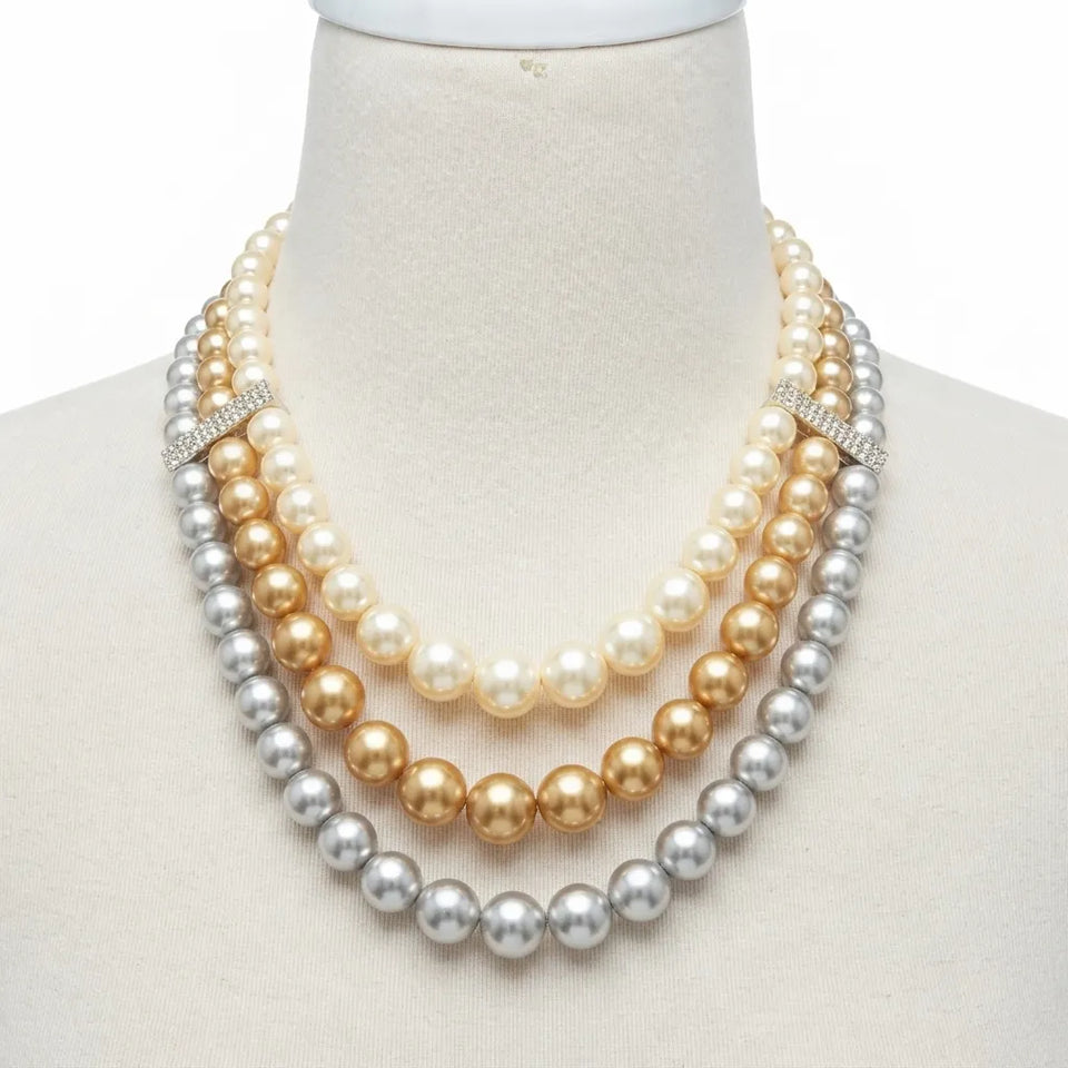 A multi-strand pearl necklace displayed on a cream-colored mannequin bust. The necklace features three strands: one strand of cream pearls, one strand of champagne-gold pearls, and one strand of silver-gray pearls, accented by silver-toned links with small clear crystals.