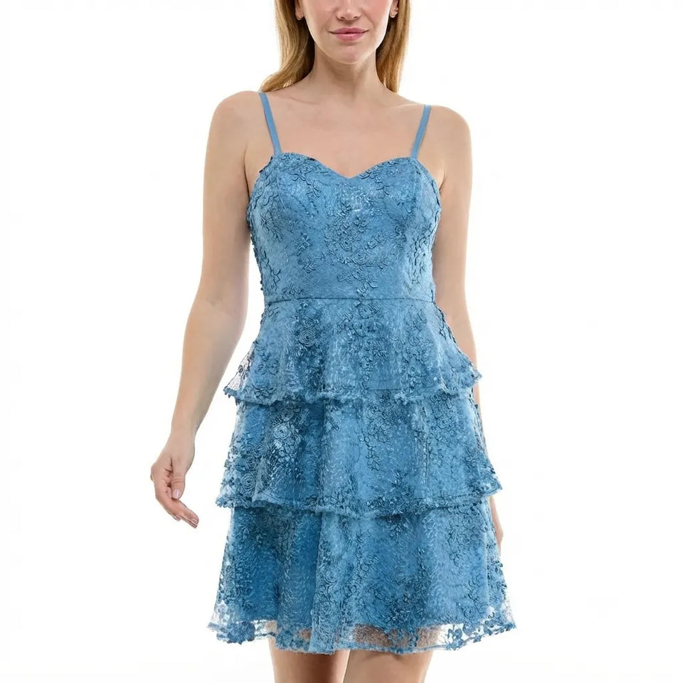 A woman wearing a light blue lace spaghetti-strap mini dress with a tiered ruffle skirt, shown against a plain white background.