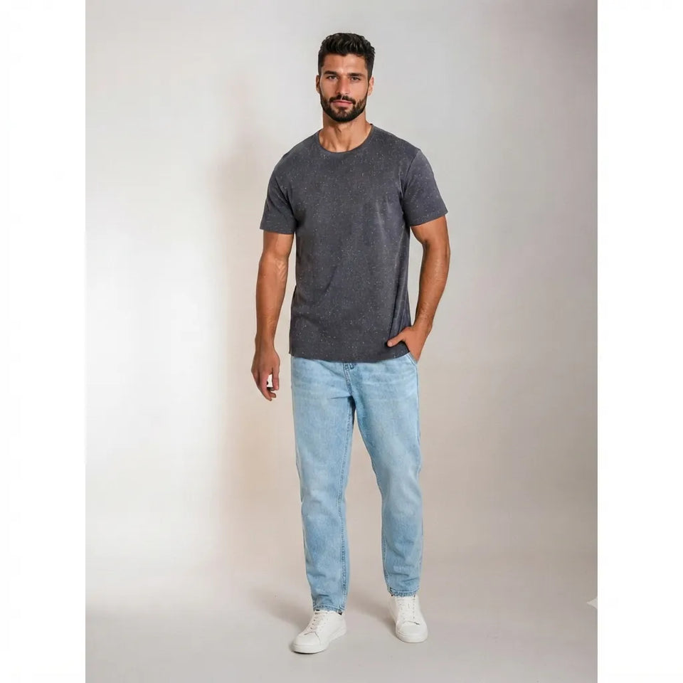A man modeling a dark gray heathered short-sleeve crewneck t-shirt, paired with light blue jeans and white sneakers, standing against a neutral light gray studio background.