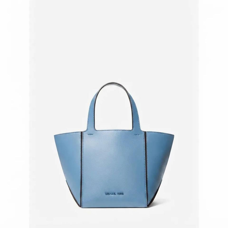 A light blue leather tote bag with structured geometric sides and double top handles, shown against a plain light gray background.