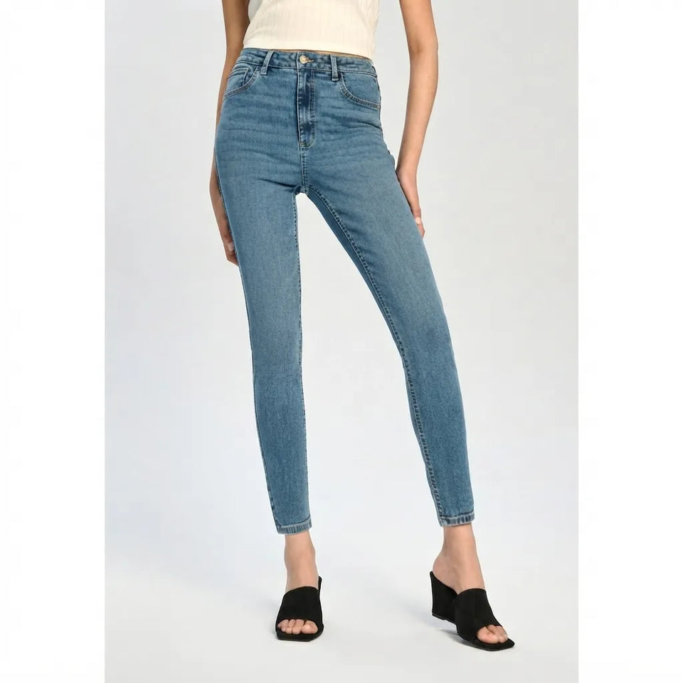 A model wearing light blue high-waisted skinny jeans with a faded wash, styled with a cream top and black slide sandals against a light gray studio background.