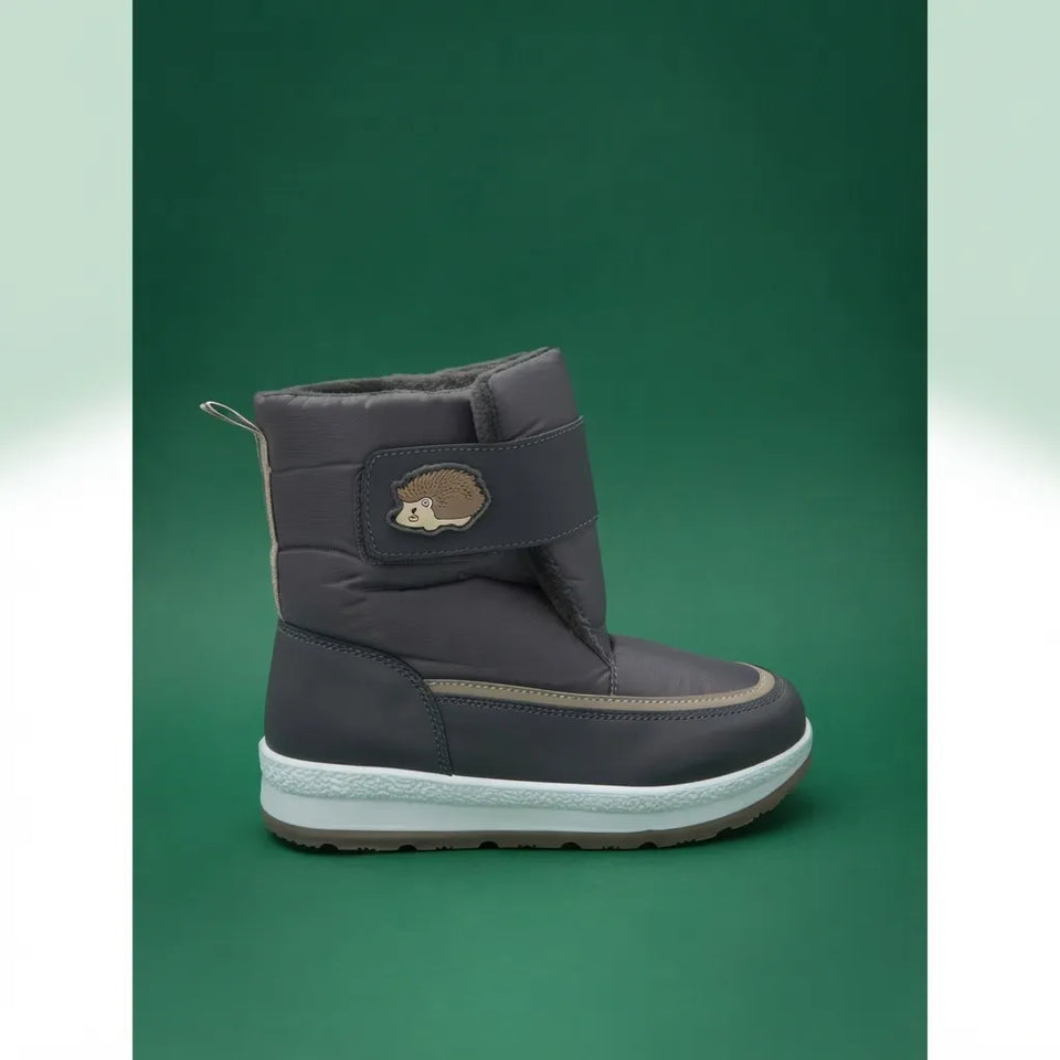 A dark gray winter boot with a padded ankle strap featuring a small hedgehog patch, set against a solid green background.