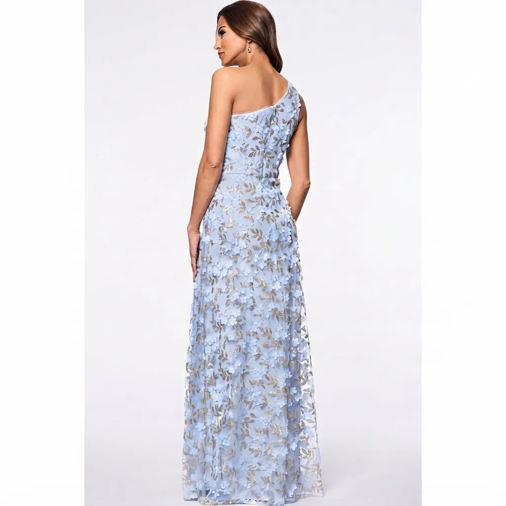 A woman modeling a floor-length one-shoulder gown with a light blue and silver floral lace pattern, shown from a three-quarters back view against a plain white studio background.