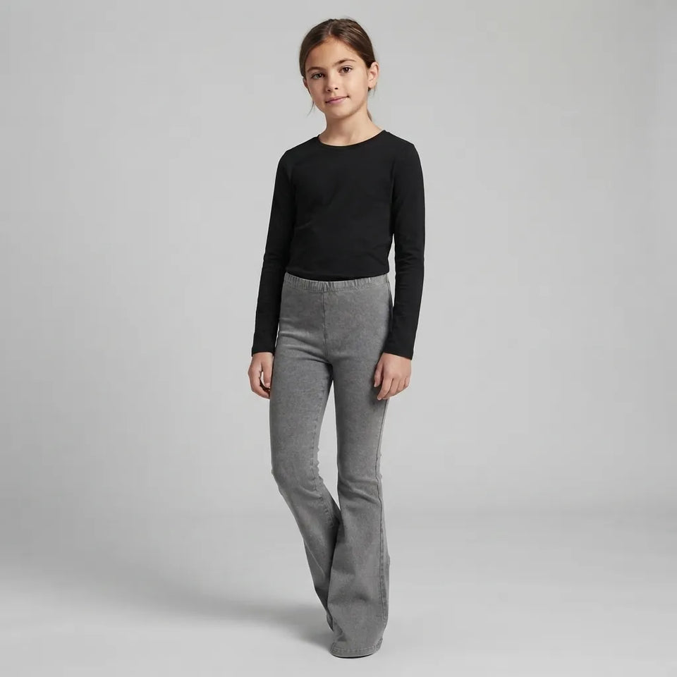 A young girl modeling a black long-sleeve crewneck top and gray flared pants against a light gray studio background.