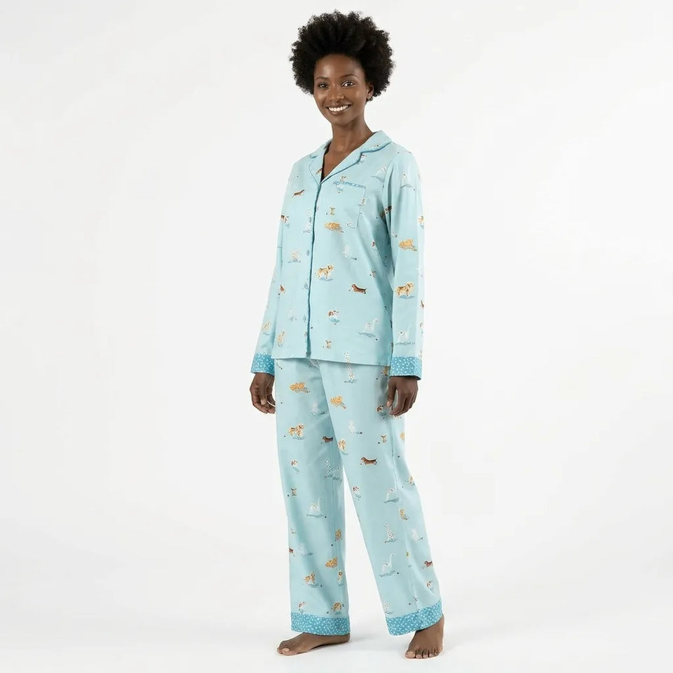 A woman modeling a light blue pajama set with a dog print, featuring a long-sleeve button-up top and matching pants, set against a plain white studio background.