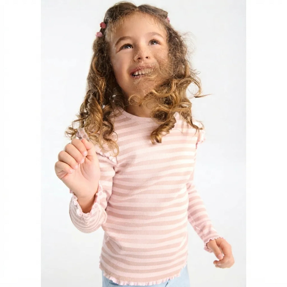 A young girl with curly brown hair wearing a light pink and white horizontally striped long-sleeve shirt, smiling and looking upwards against a plain white background.
