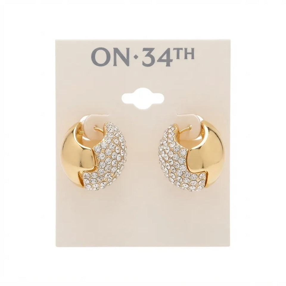 A pair of gold crescent-shaped hoop earrings with pavé crystal detailing, displayed on a beige card labeled 'ON 34TH' against a white background.