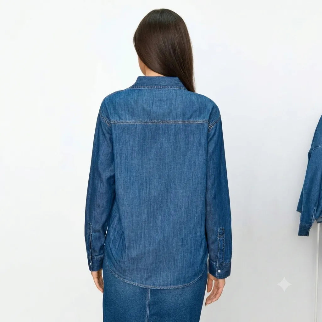 A woman viewed from the back wearing a blue denim button-up shirt and matching denim skirt against a plain white studio background.