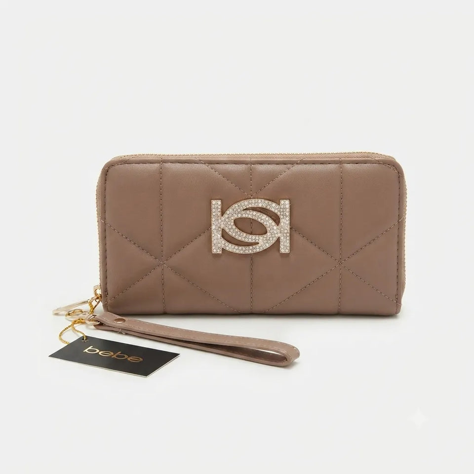 A taupe quilted zip-around wallet with a wristlet strap and a rhinestone-embellished HK logo on the front, shown with a black Bebe brand tag on a light gray background.