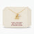 A gold necklace with a letter 'A' pendant and a small heart-shaped cubic zirconia charm, displayed on a cream-colored jewelry card with text detailing the materials.