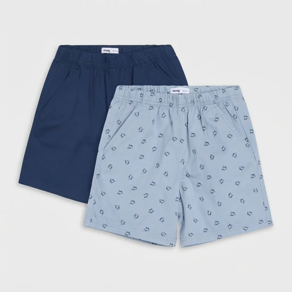 Two pairs of boys' shorts from the brand Longchamp, displayed flat against a light gray background. The pair in the back is solid navy blue, and the pair in the front is light blue with a small repeating anchor pattern.