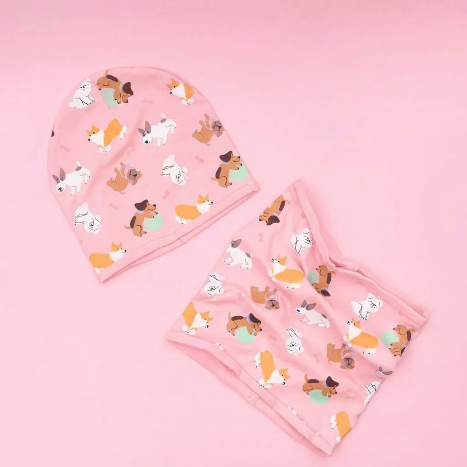 A pink baby bonnet and matching diaper cover set with a playful pattern of cartoon dogs, corgis, and foxes in white, brown, and orange, displayed on a solid pink background.