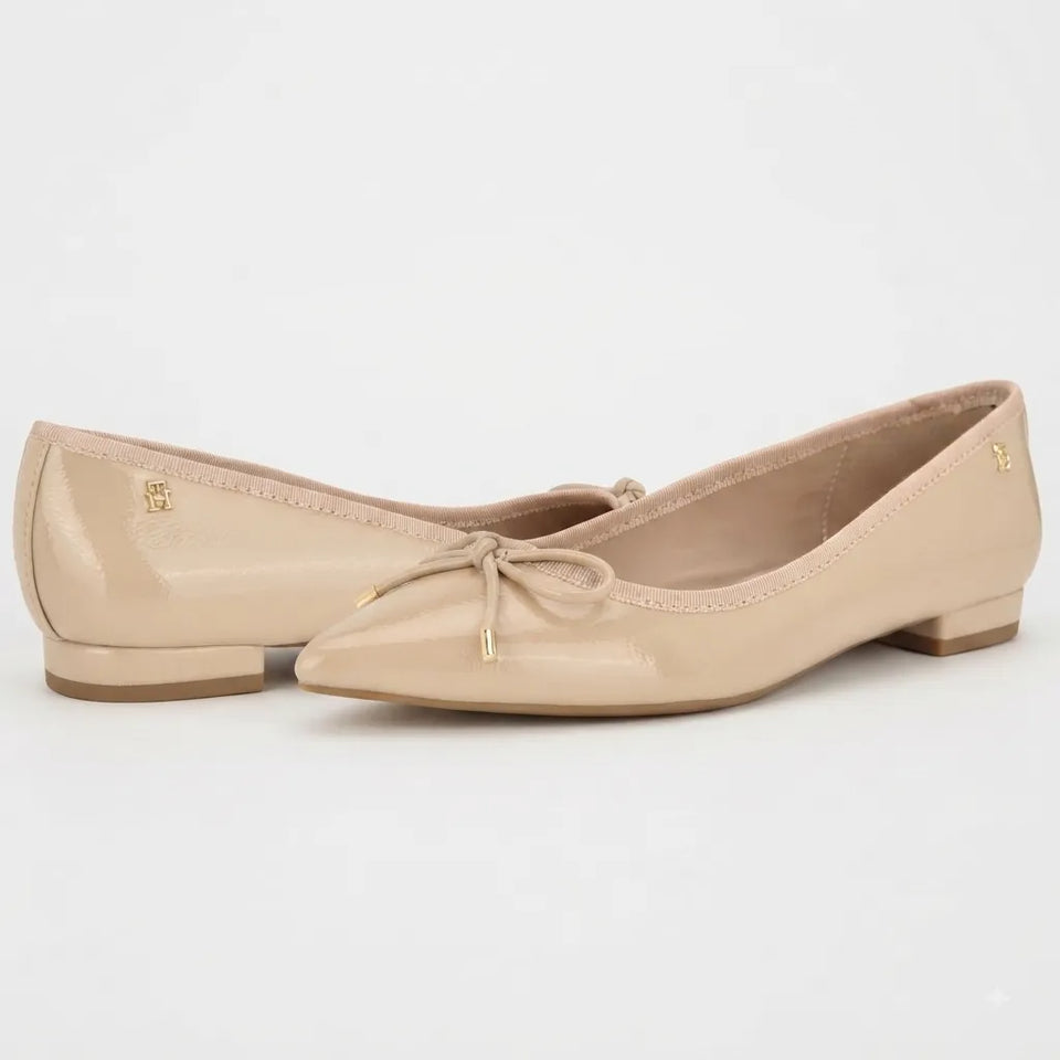 A pair of beige patent leather ballet flats with pointed toes, delicate bow details on the fronts, and small gold logo accents on the sides, set against a plain white background.